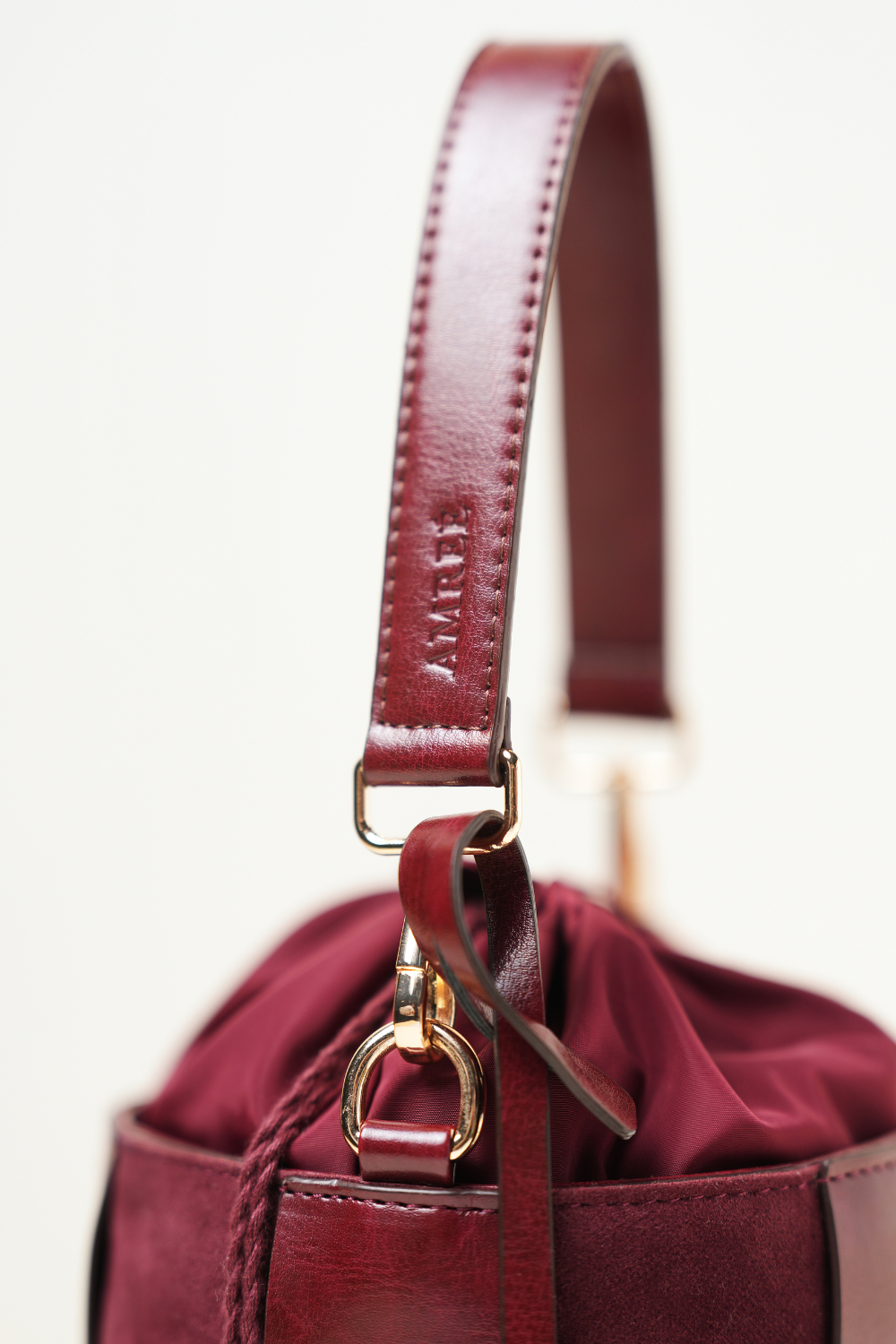 Derby Bucket Bag Burgundy displayed with its adjustable shoulder strap showing versatile carry options.