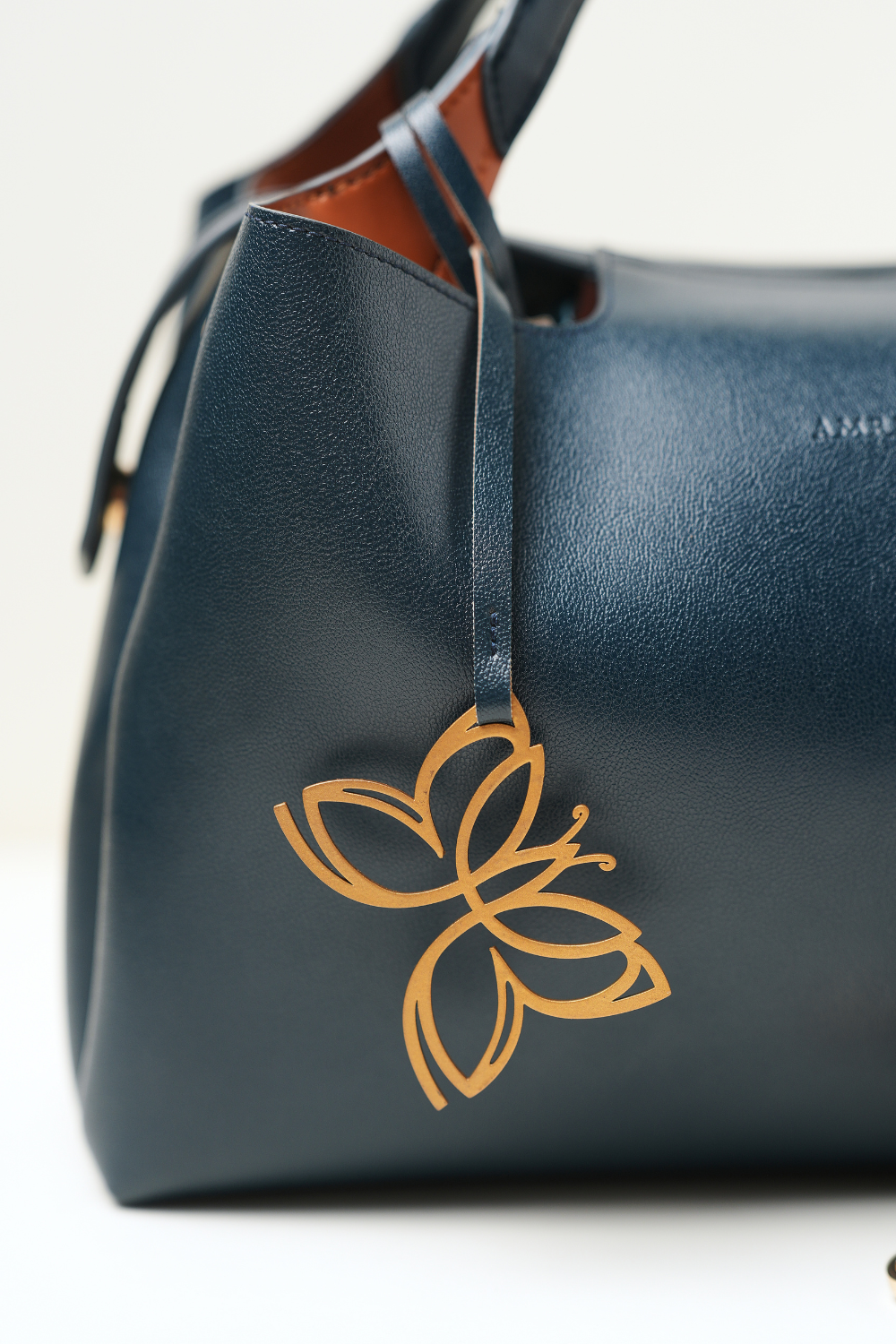 Close-up of the Equitana Top Handle Navy handbag showing the Amrée logo detailing on the front.