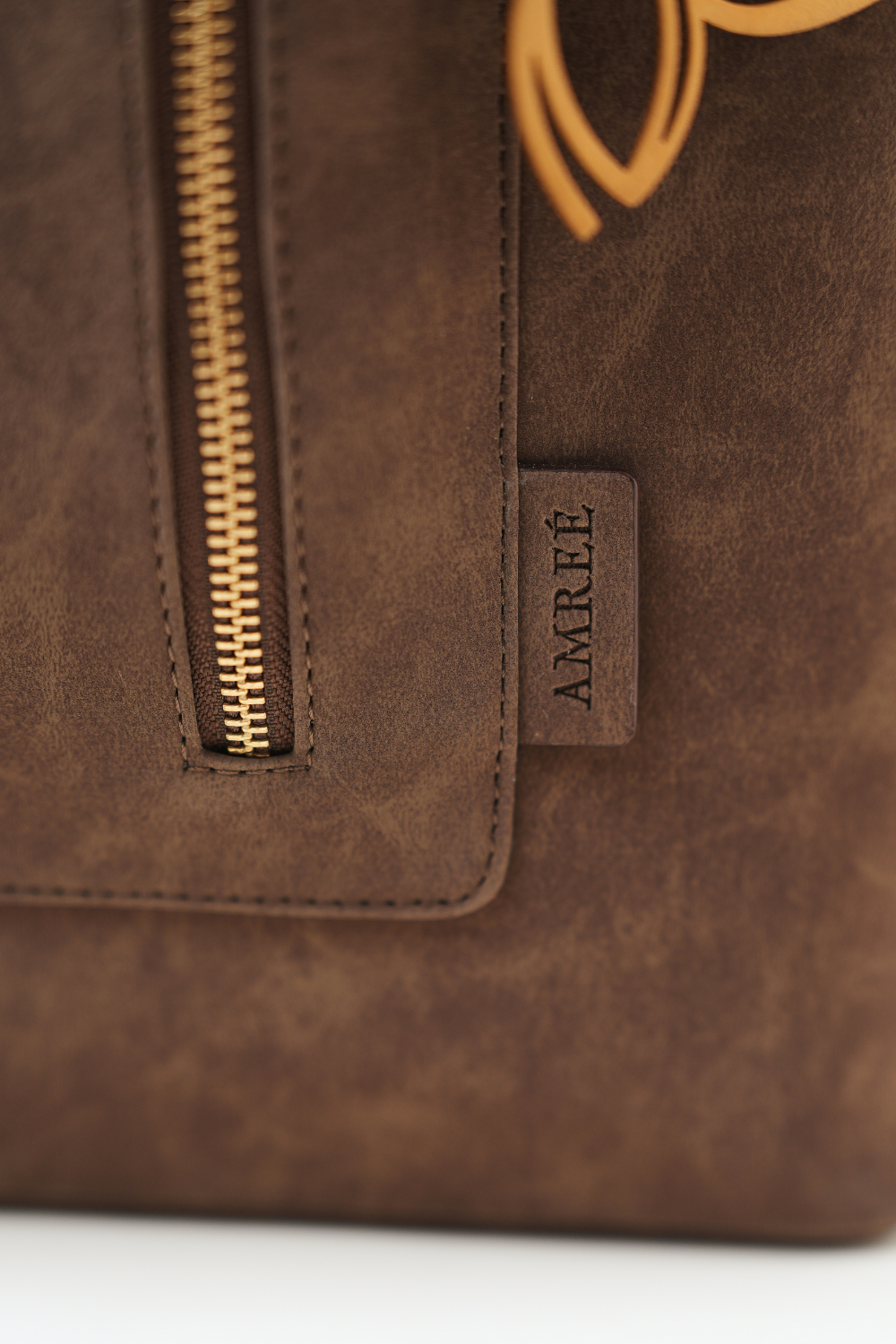 Close-up of the Rodeo Totepack Brown showing the Amrée brand tag, fine stitching, and textured material detailing.
