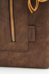 Close-up of the Rodeo Totepack Brown showing the Amrée brand tag, fine stitching, and textured material detailing.