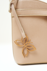 Close-up of the Rosette Sling Beige showing the Amrée butterfly emblem with fine metal detailing and clean stitching.
